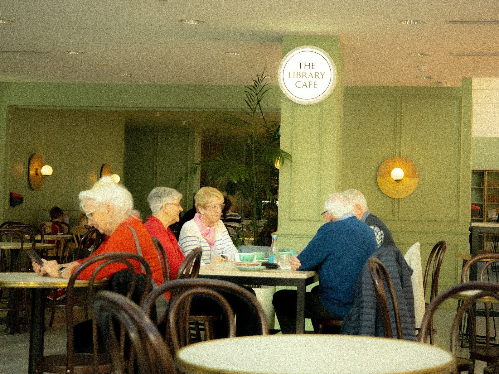 Pessoas sentadas a mesas em um café com paredes verdes e luminárias redondas