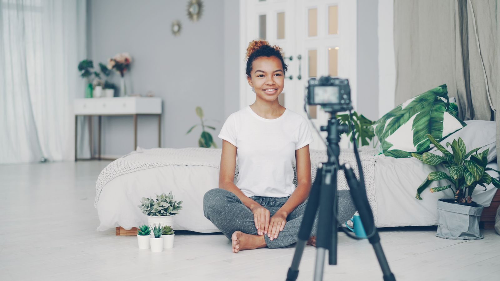 Mulher sorridente gravando um vlog em ambiente interno aconchegante com plantas e luz suave