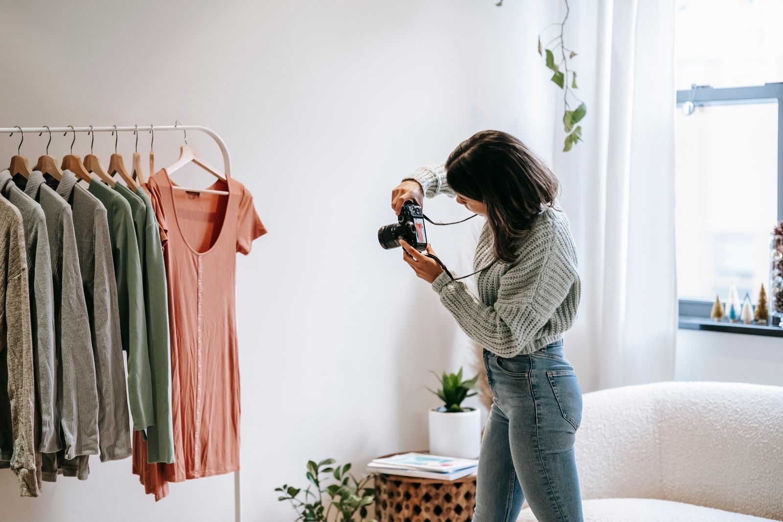 Jovem fotógrafa de roupa casual fotografando uma camisa em cabide em apartamento moderno