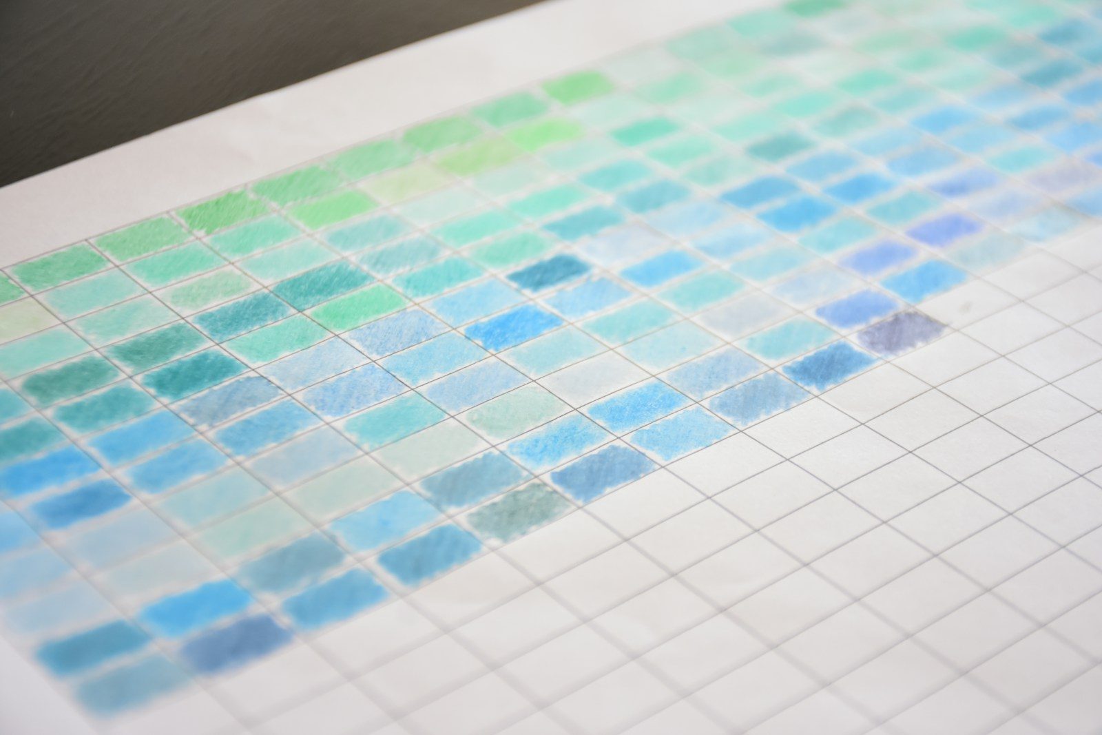 Grade de amostras de cor pintadas à mão, do verde ao azul, em papel branco