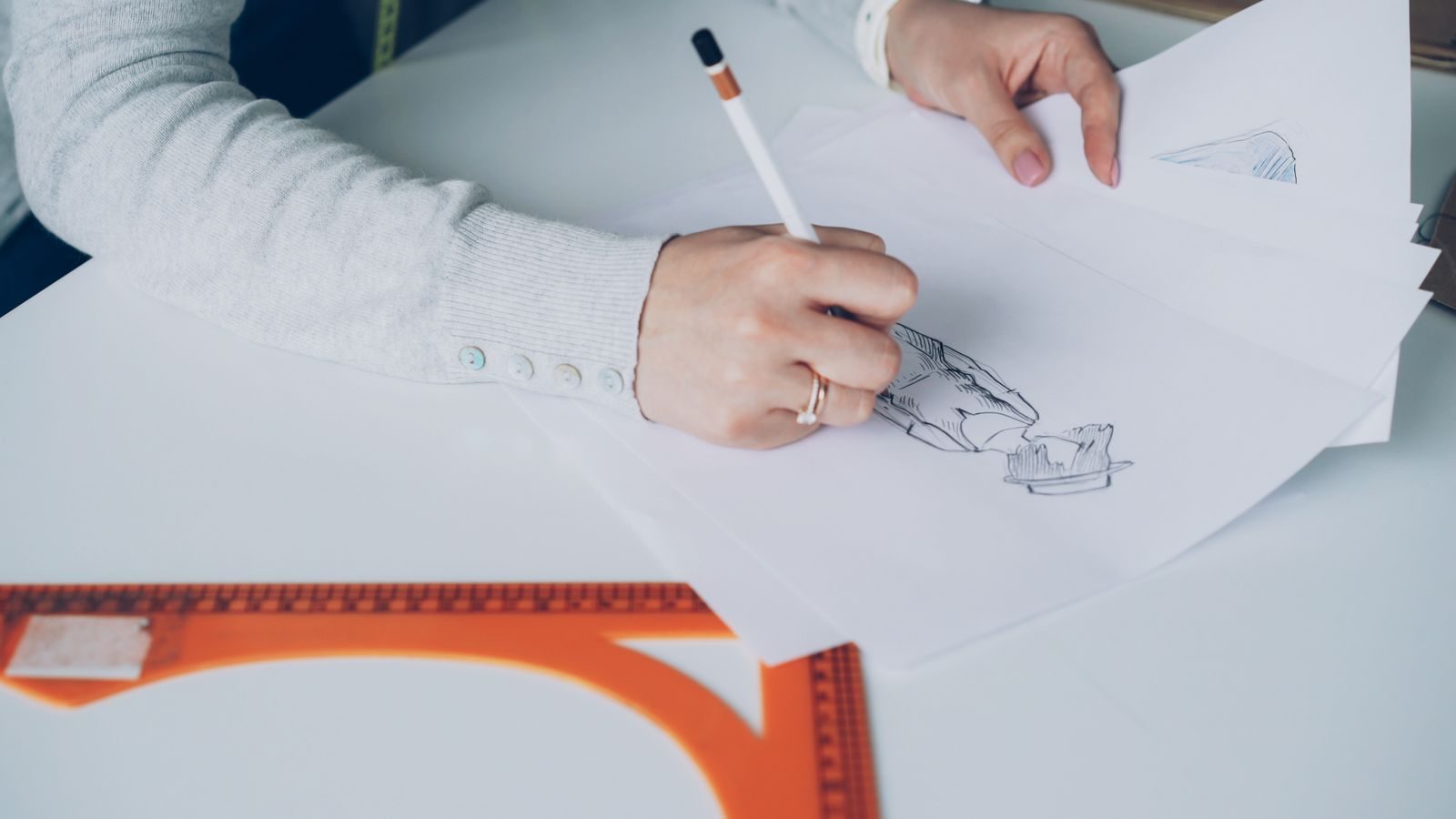 Close de artista criando croquis de moda sentada a uma mesa em ambiente interno
