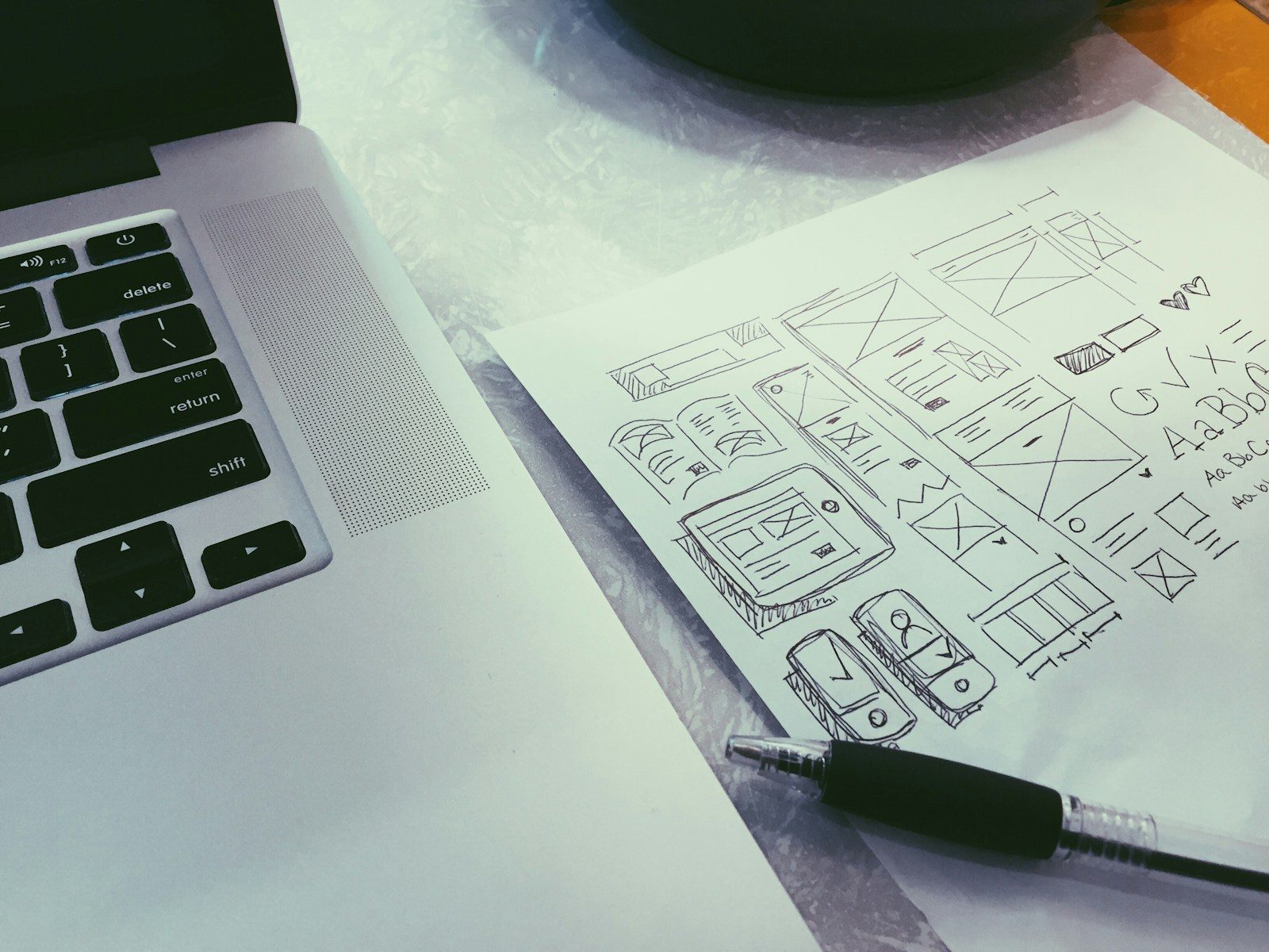 Caneta esferográfica sobre papel ao lado de um MacBook