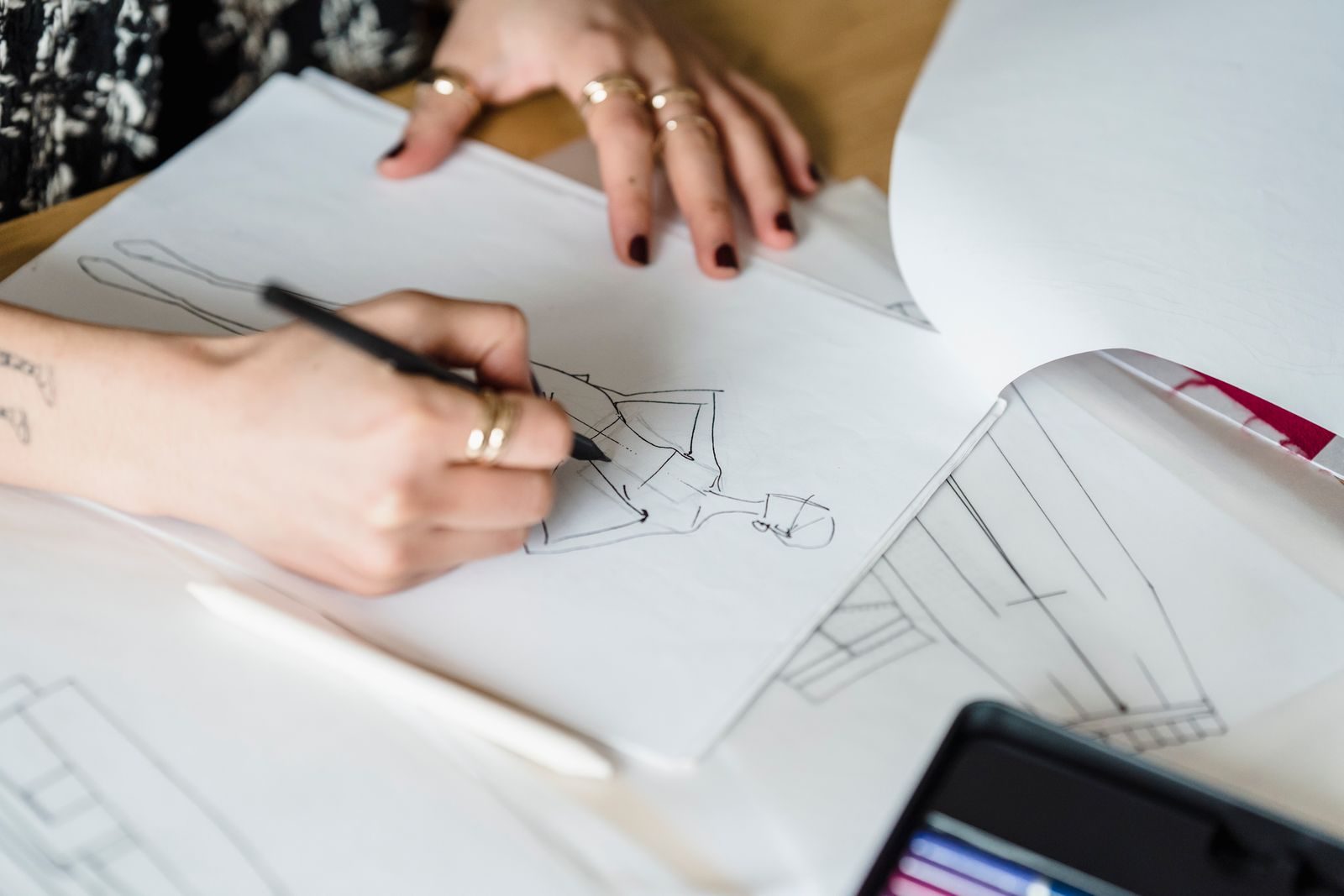 Vista de cima de designer anônima desenhando o esboço de uma roupa em mesa com papéis num ateliê claro