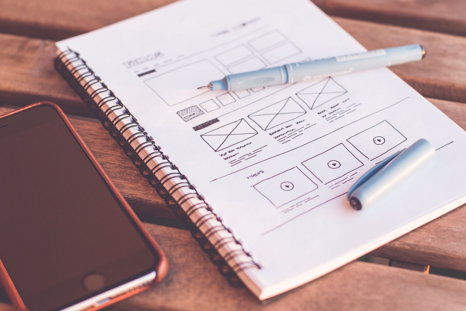 Close de caderno com esboços de wireframe e smartphone em mesa de madeira