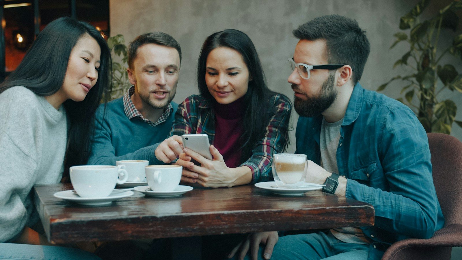 Quatro pessoas olhando juntas para um smartphone em mesa de madeira de um café