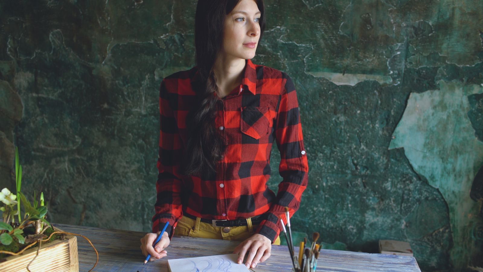 Mulher de camisa xadrez vermelha desenhando em uma mesa de madeira