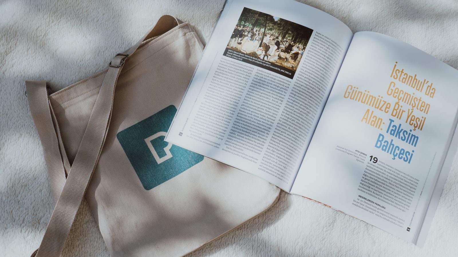 Vista de cima de bolsa tote e revista aberta sobre fundo texturizado com luz natural suave