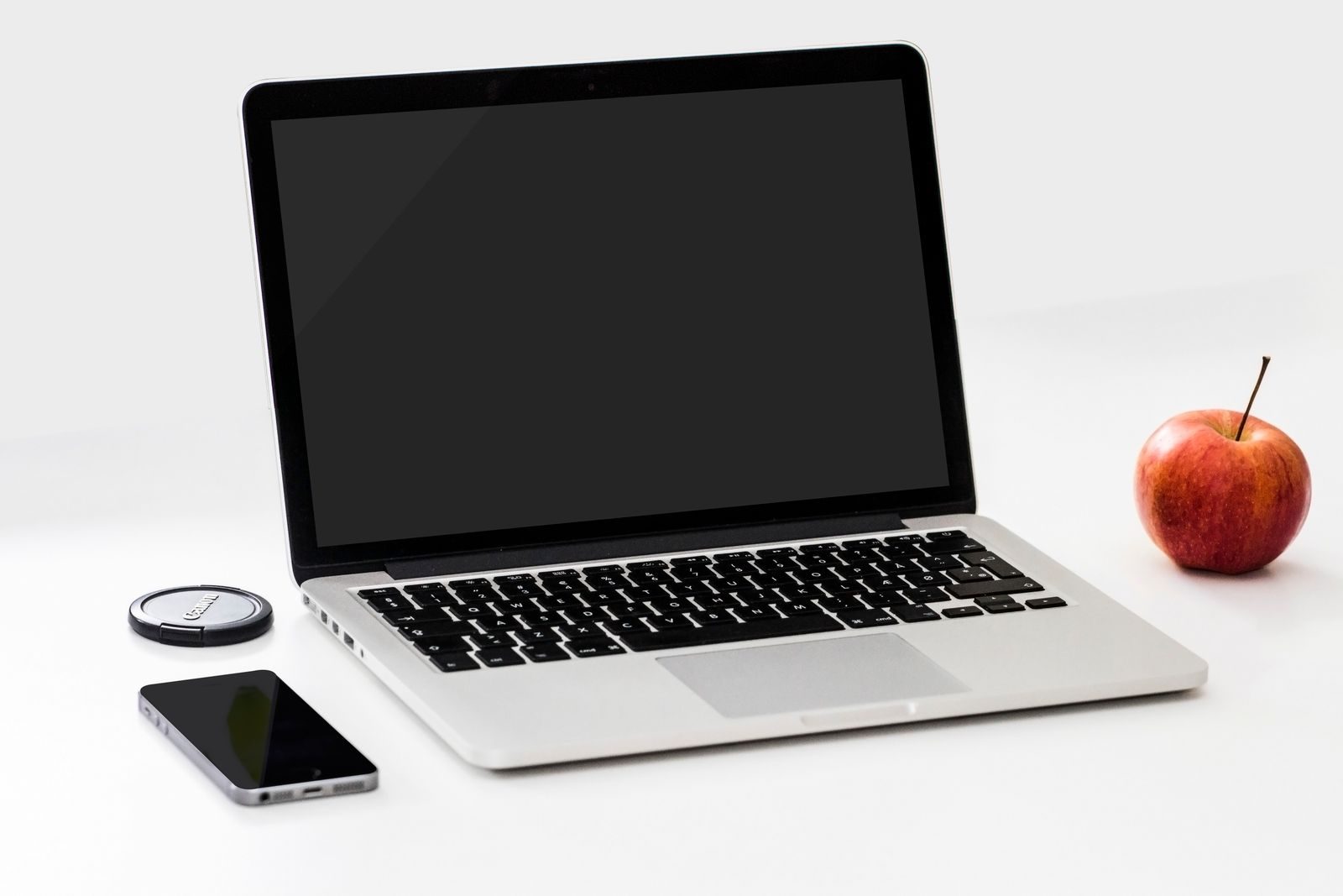 Espaço de trabalho minimalista com notebook, smartphone e uma maçã em mesa branca