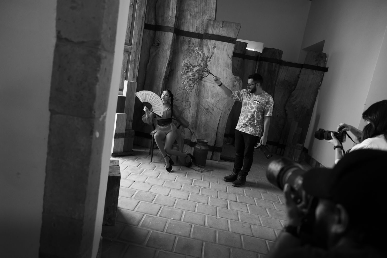 Cena artística em estúdio com fotógrafos e modelo posando com ventilador em preto e branco
