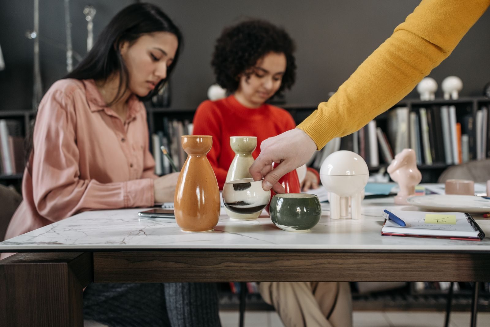 Mulheres colaborando em um escritório estiloso com cerâmicas e anotações na mesa