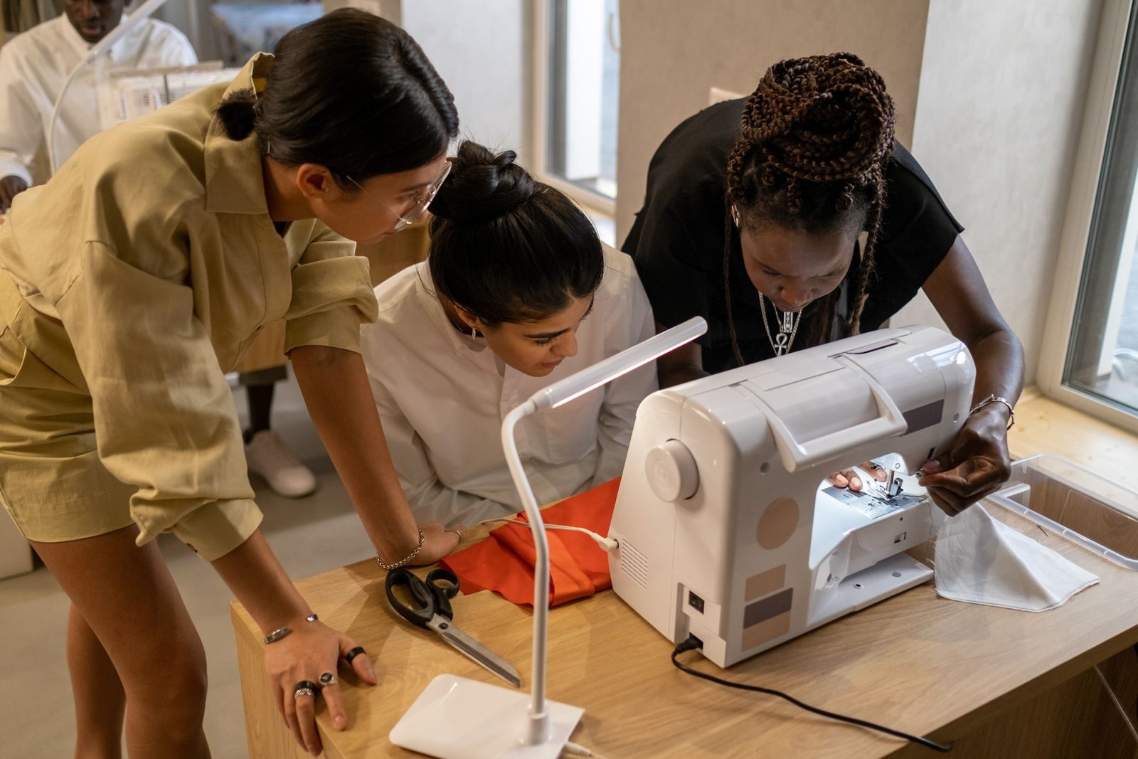 Três estilistas diversos trabalhando juntos em uma máquina de costura em um ateliê criativo