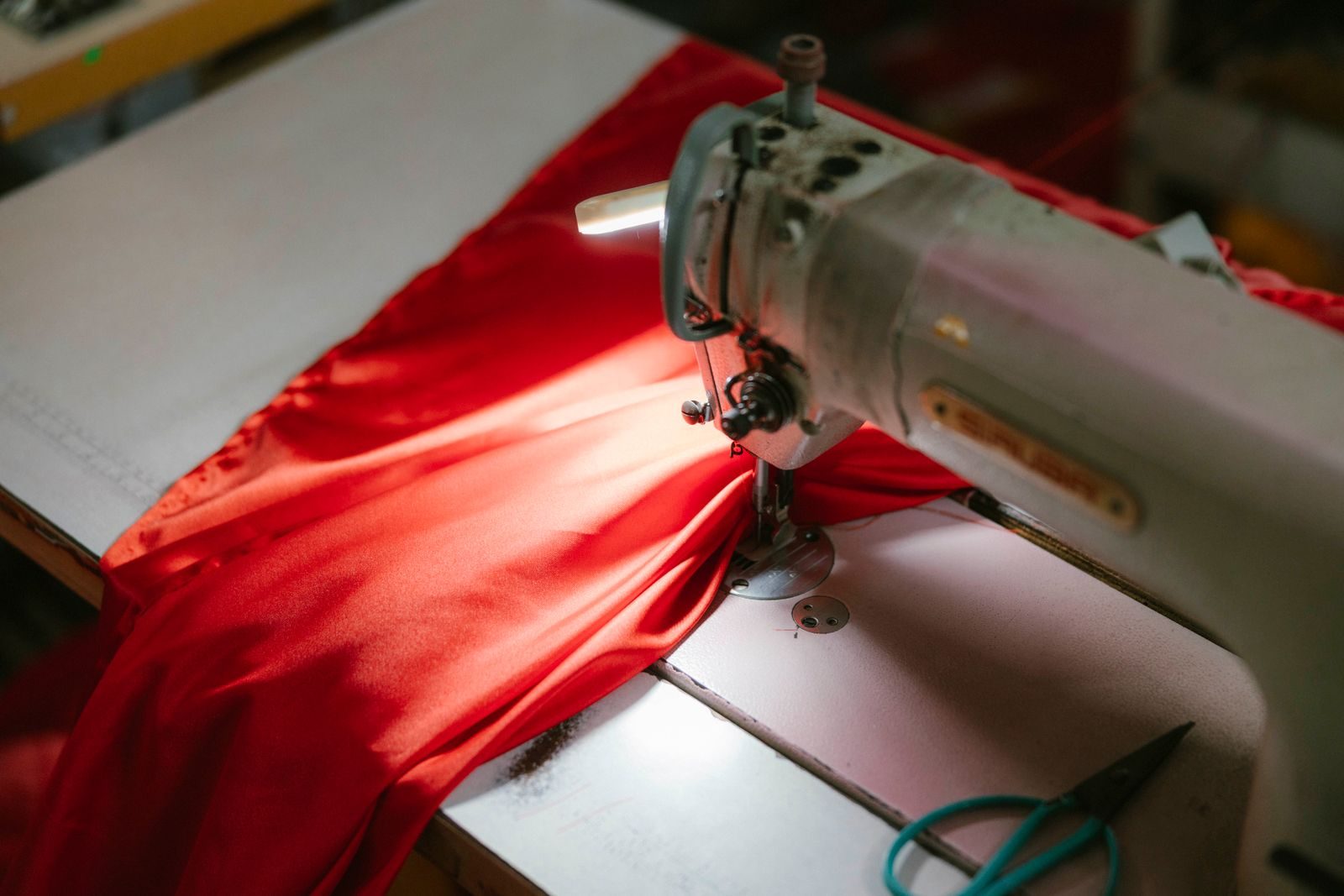 Close de máquina de costura industrial costurando tecido vermelho vivo sob um foco de luz