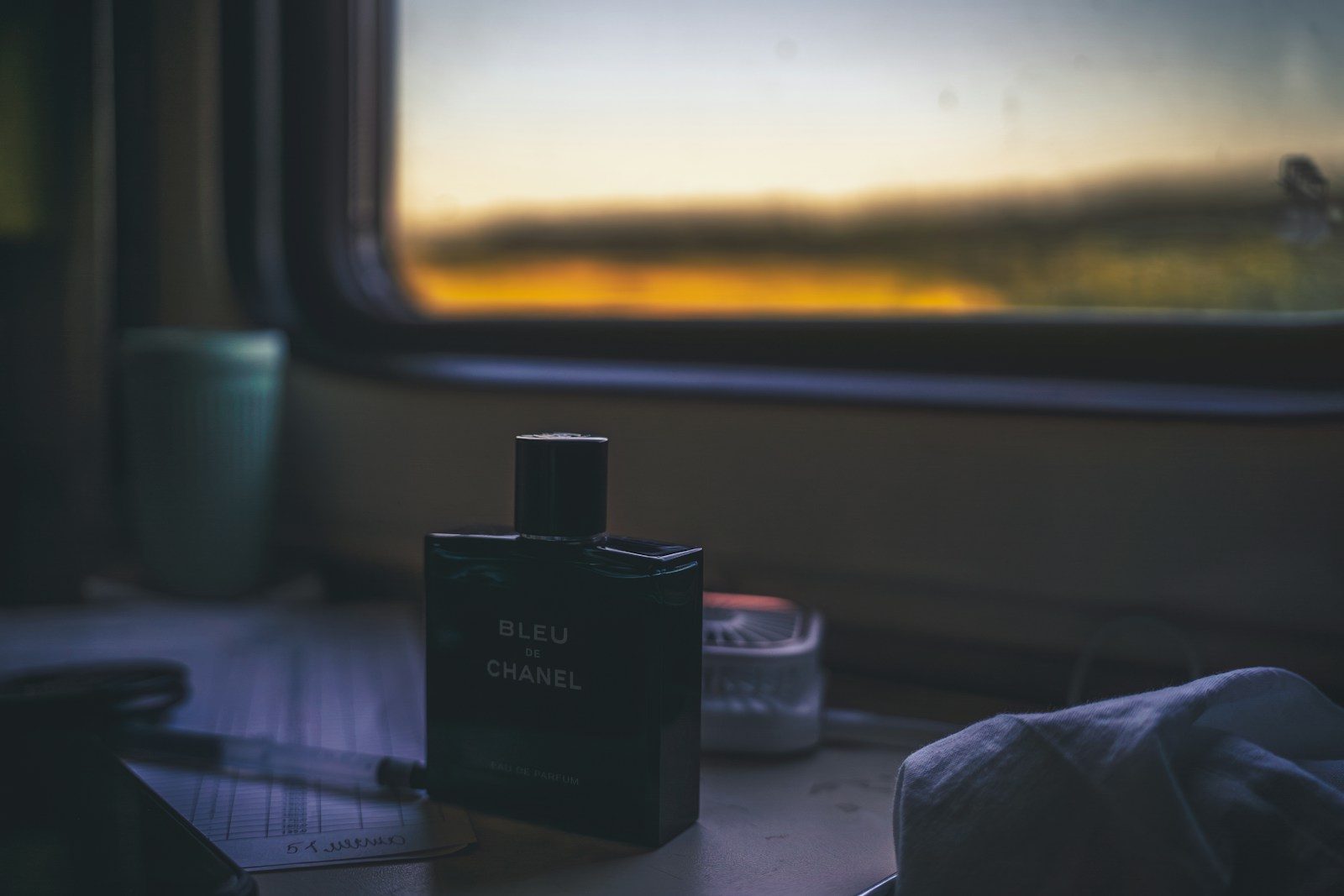 Frasco de perfume escuro junto a uma janela ao pôr do sol