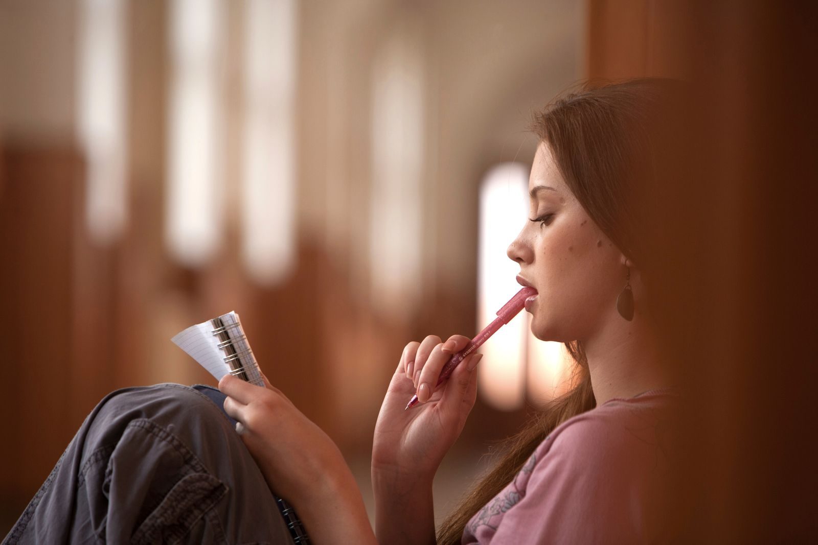 Jovem pensativa segurando caneta e caderno em ambiente interno