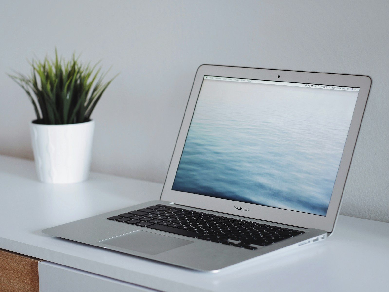 MacBook Air ao lado de uma planta verde sobre superfície de madeira branca