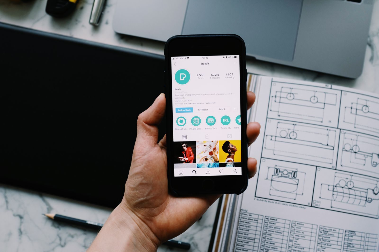 Mão segurando smartphone com perfil de rede social e aparelhos eletrônicos na mesa