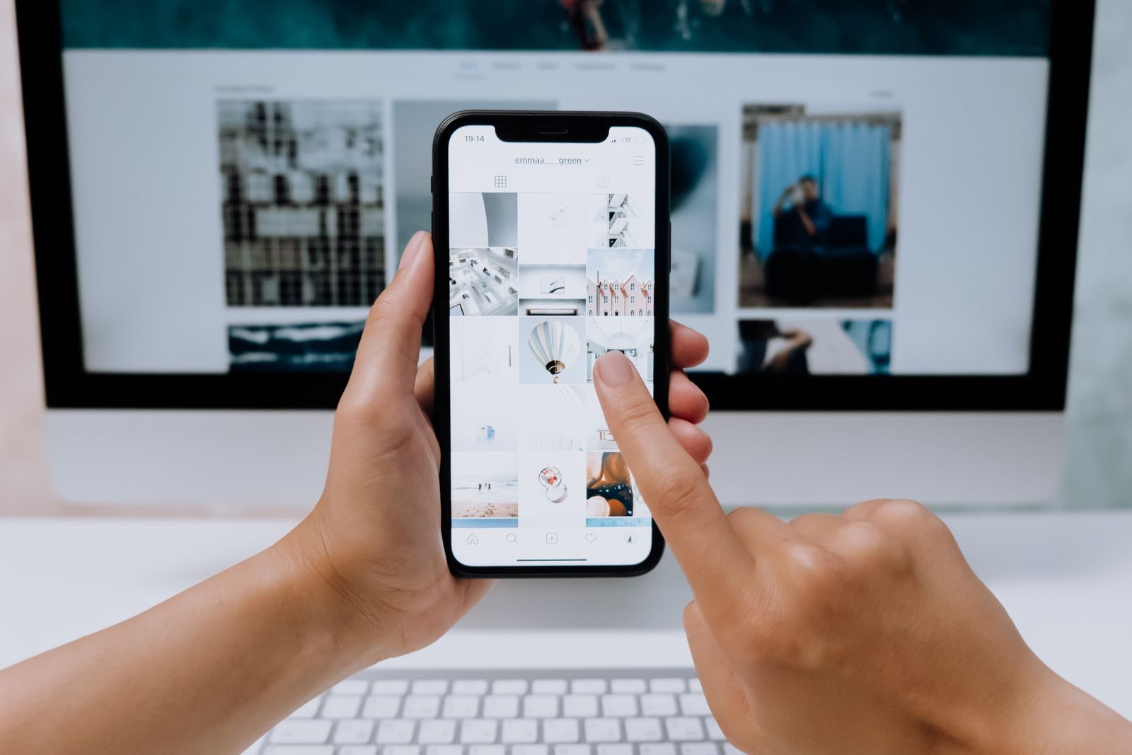 Mãos segurando smartphone em app de rede social diante de um computador de mesa