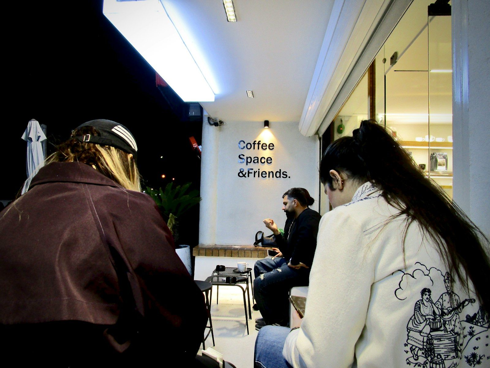 Pessoas reunidas em frente a uma cafeteria à noite