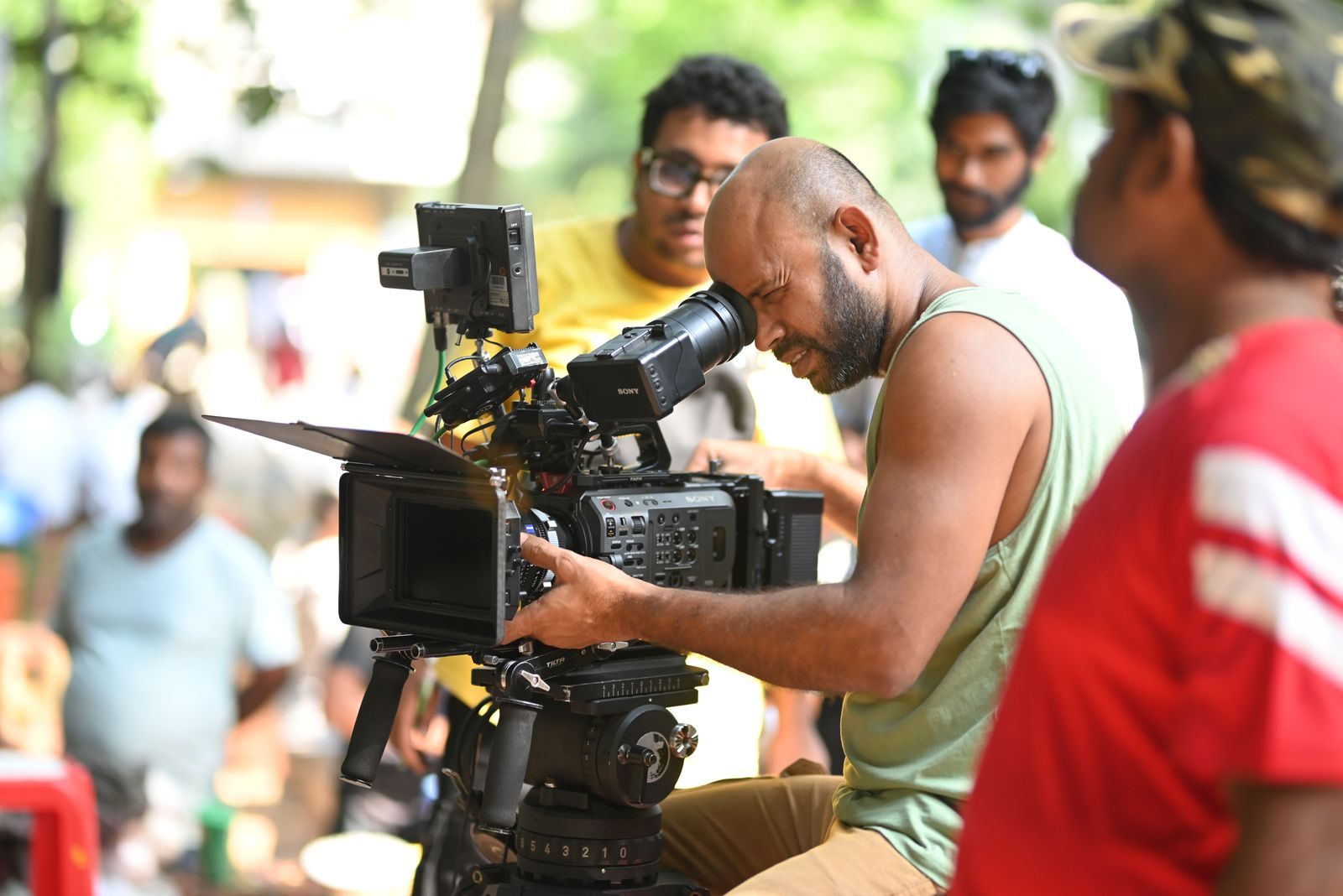 Cineasta usando uma câmera de vídeo profissional em um set externo, cercado pela equipe