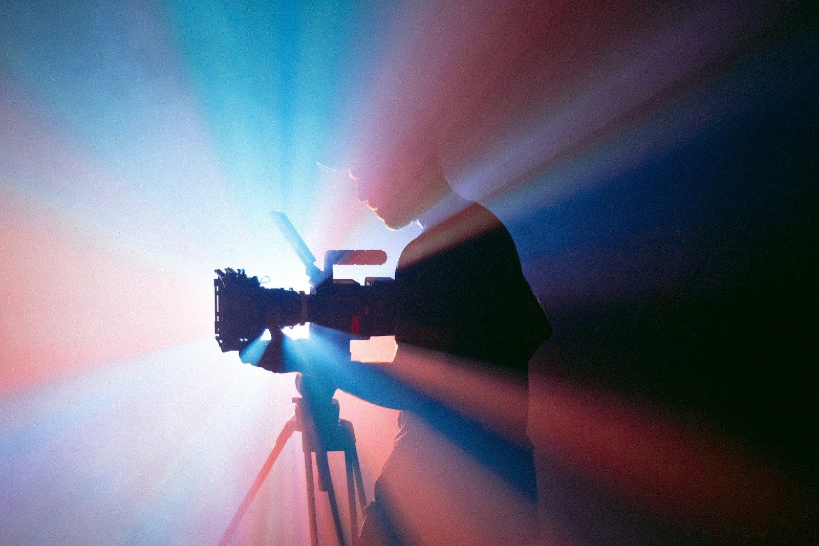 Pessoa filmando com uma câmera em um tripé sob luz azul e vermelha