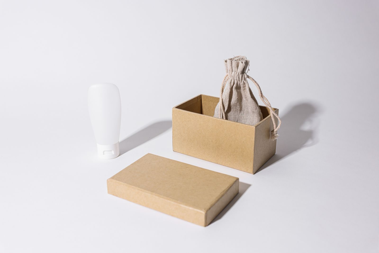 Mockup minimalista com caixa de papelão, bolsinha de linho e tubo de creme sobre fundo branco