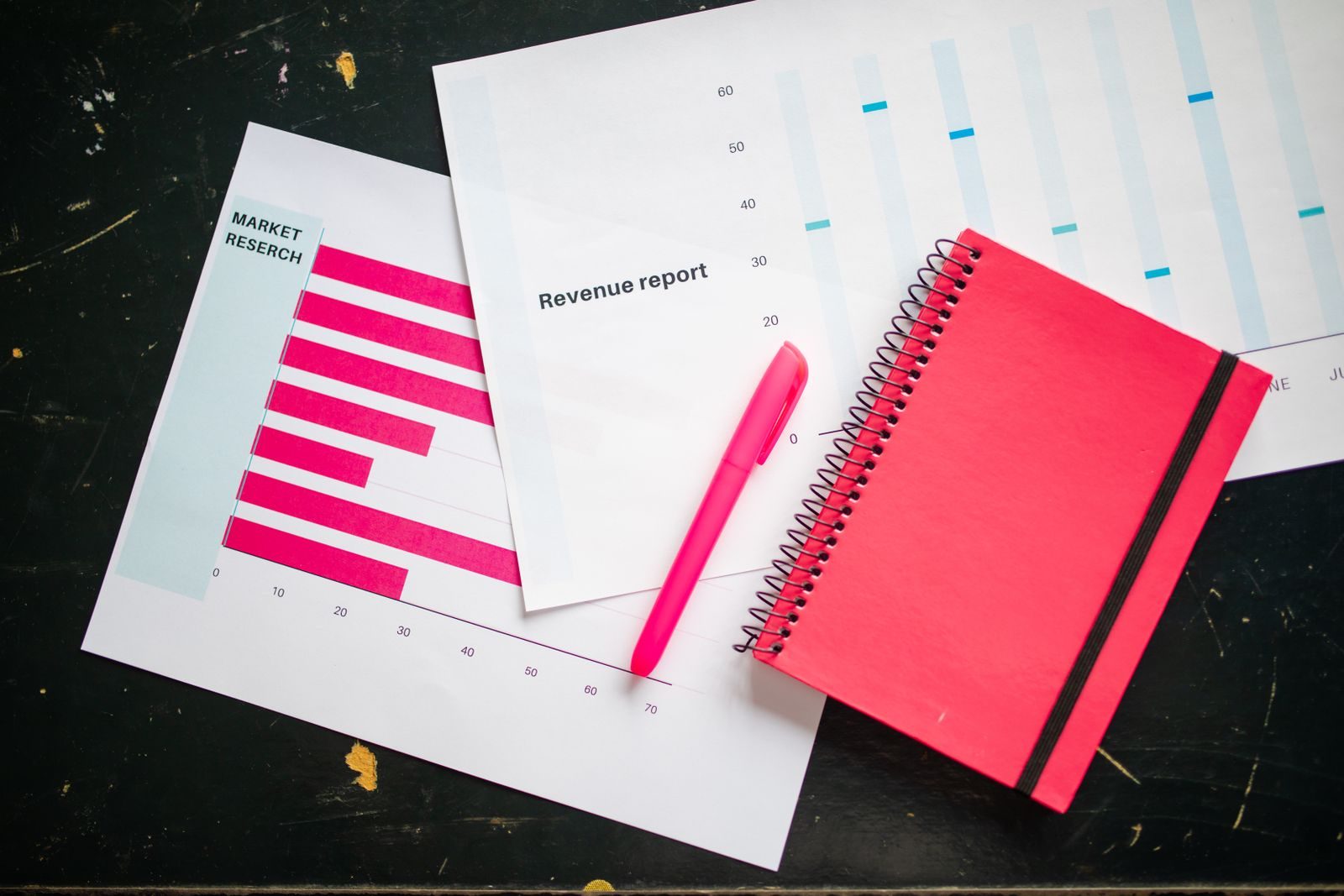 Vista de cima de uma mesa com gráficos, caderno vermelho e caneta para análise de negócios