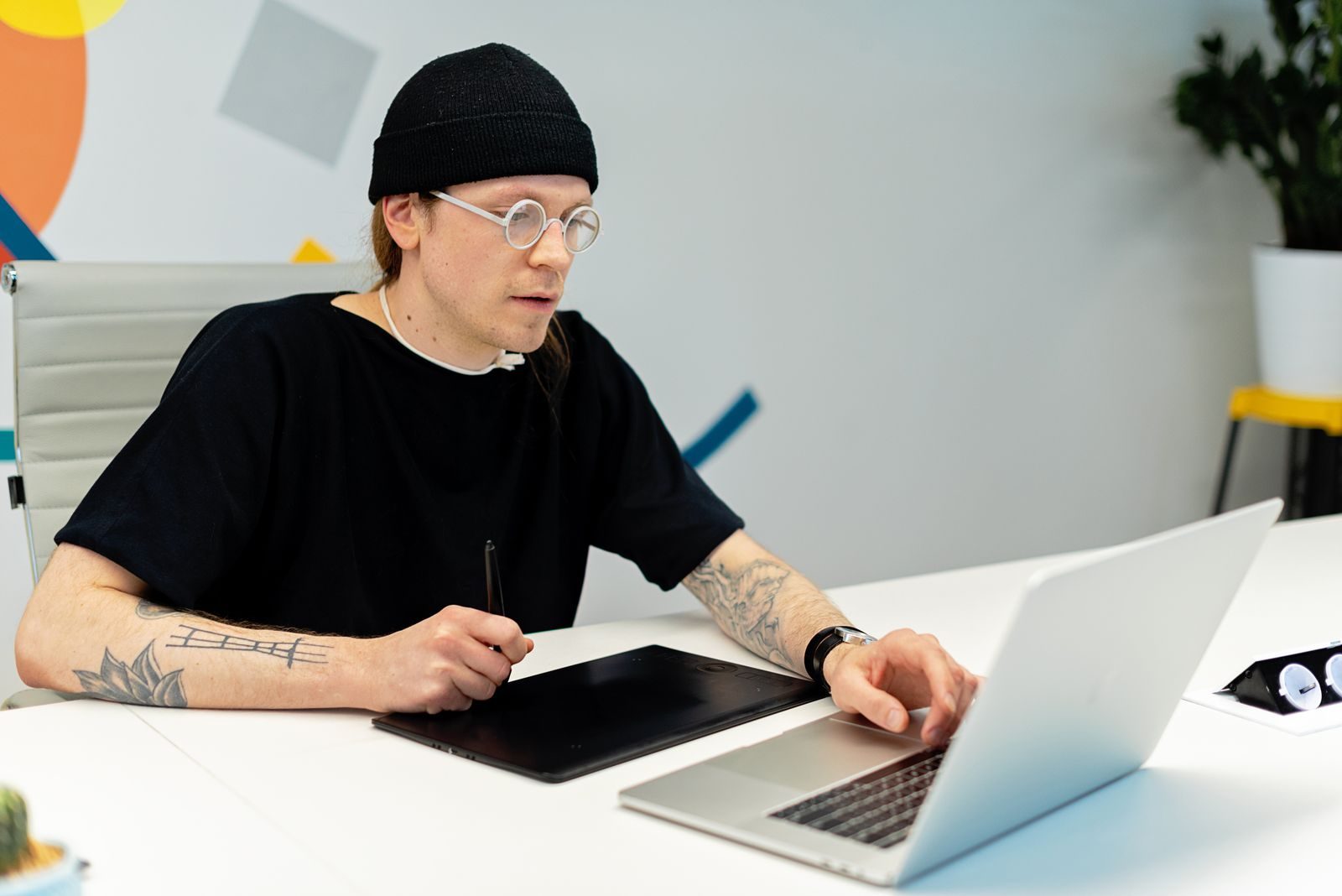 Designer tatuado trabalhando com notebook e tablet em um escritório estiloso