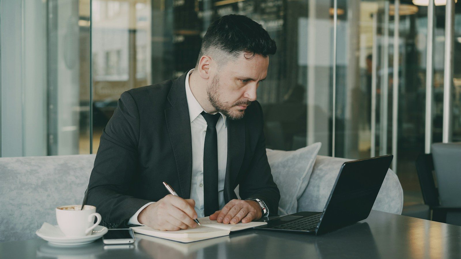 Homem de terno escrevendo em um caderno à mesa de um café