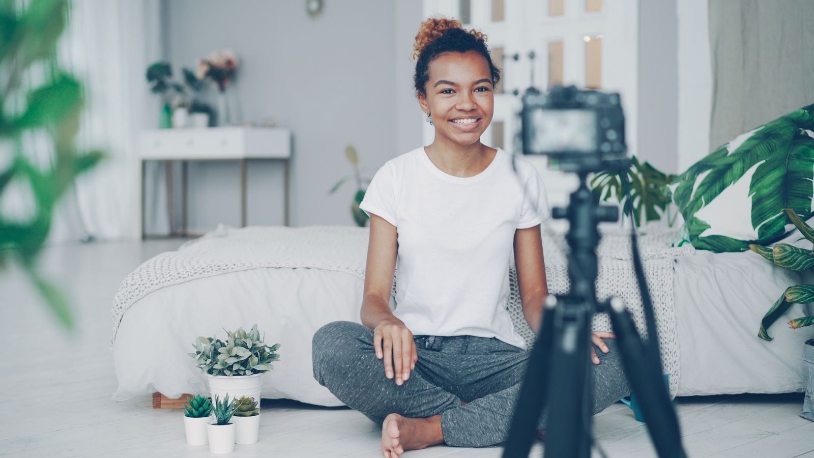 Jovem sorridente gravando vlog em casa, cercada de plantas e decoração