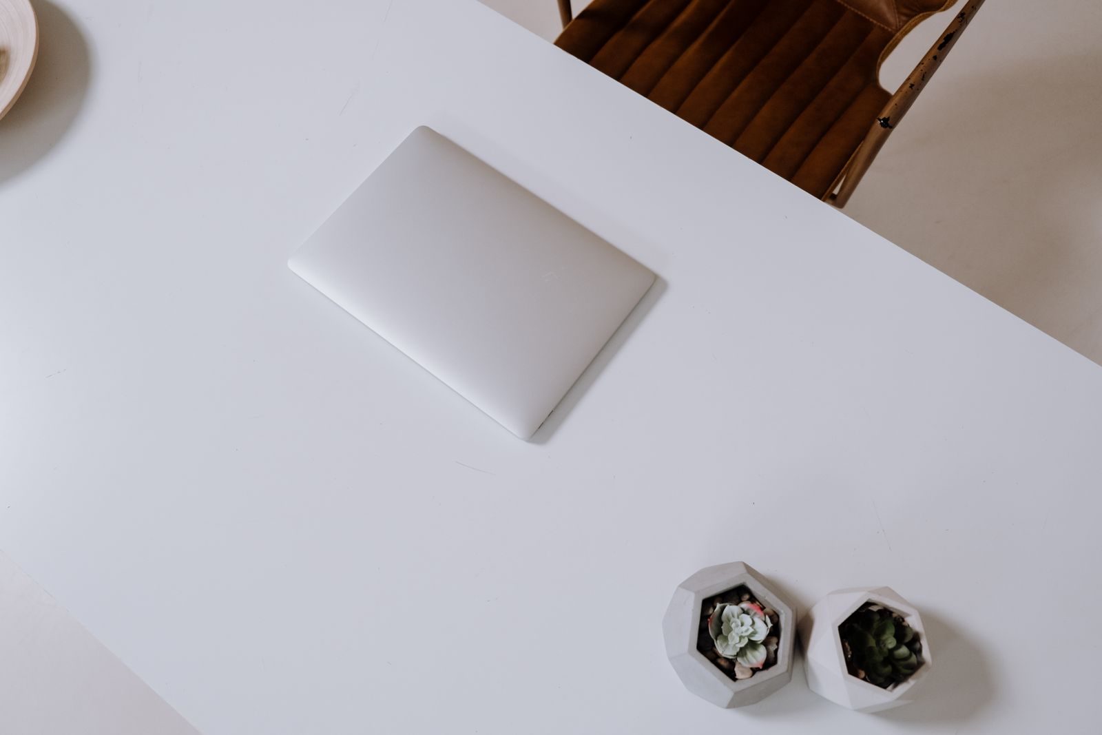 Mesa branca moderna e minimalista com notebook fechado e suculentas