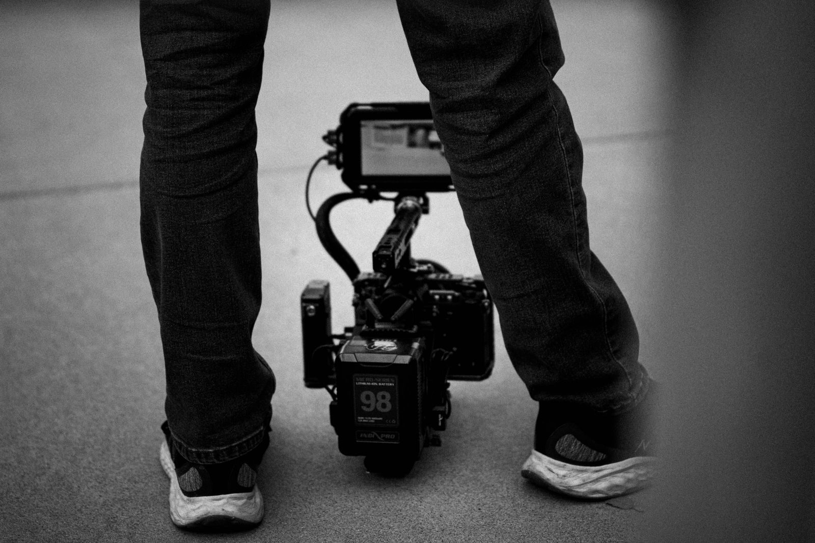 Foto em preto e branco de um cineasta em pé com uma câmera profissional no chão