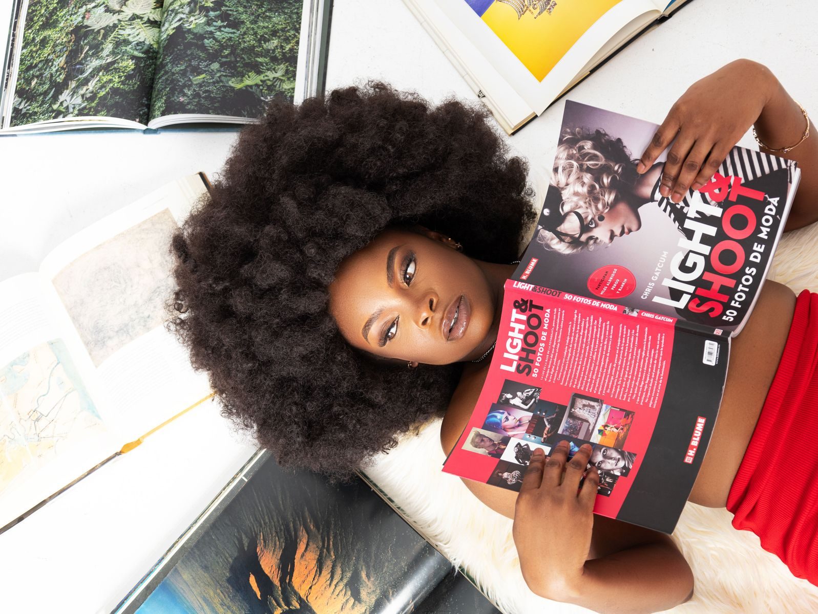Mulher elegante lendo revista de moda cercada por livros abertos