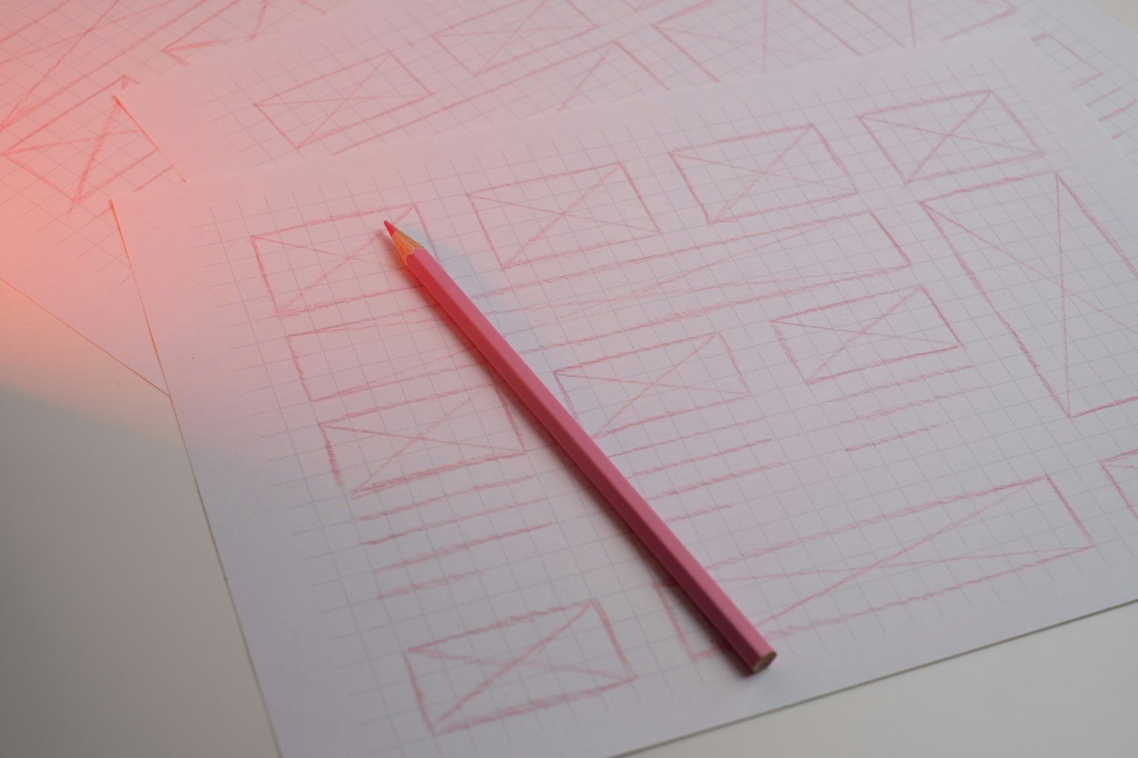 Lápis rosa sobre papel quadriculado com esboços de wireframe desenhados à mão