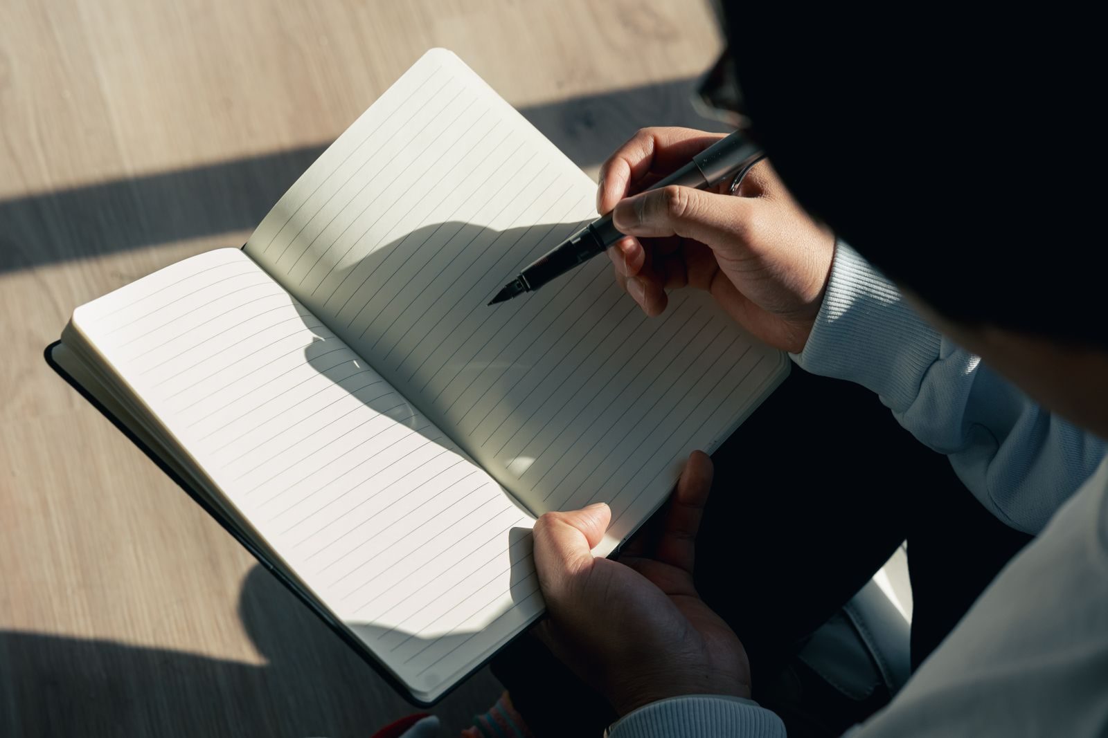 Close de pessoa escrevendo em caderno em dia ensolarado, expressando criatividade