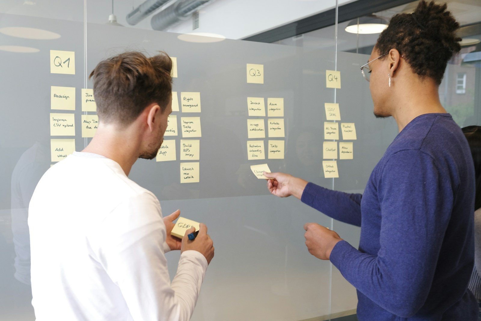 Duas pessoas planejando um projeto com post-its amarelos em uma parede de vidro