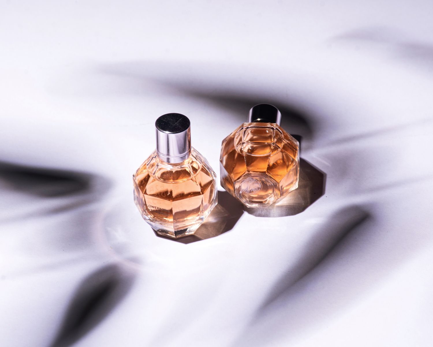 Close de dois frascos de perfume elegantes projetando sombras sobre uma superfície suave