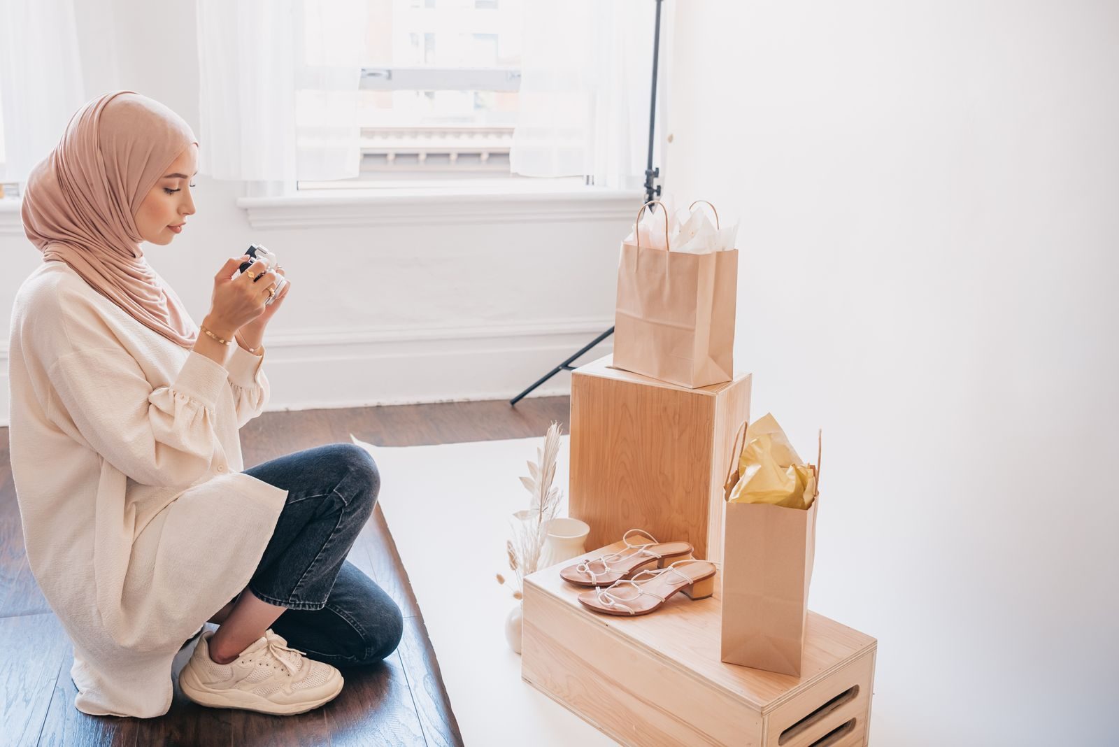 Mulher de hijab ajoelhada fotografando uma vitrine com sacolas e sapatos