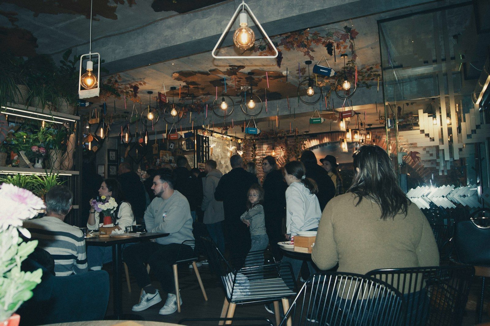 Pessoas reunidas em um café com pouca luz e luminárias pendentes