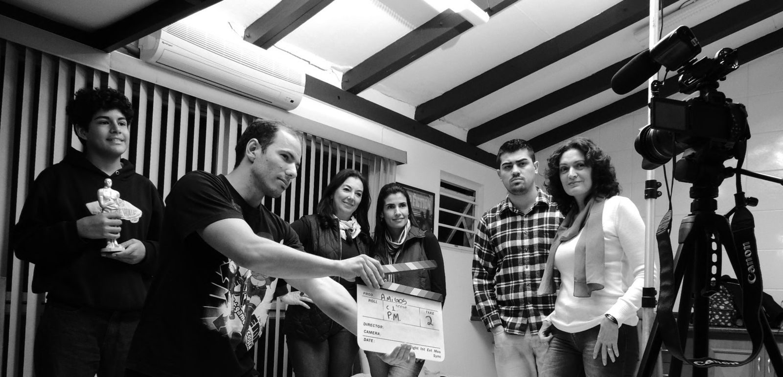 Grupo de adultos colabora em um projeto de filmagem segurando uma claquete em ambiente interno