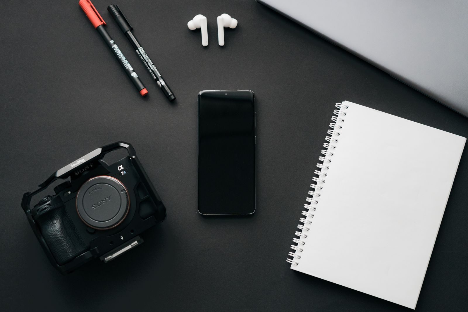 Flat lay de aparelhos modernos com câmera, smartphone e caderno sobre superfície preta