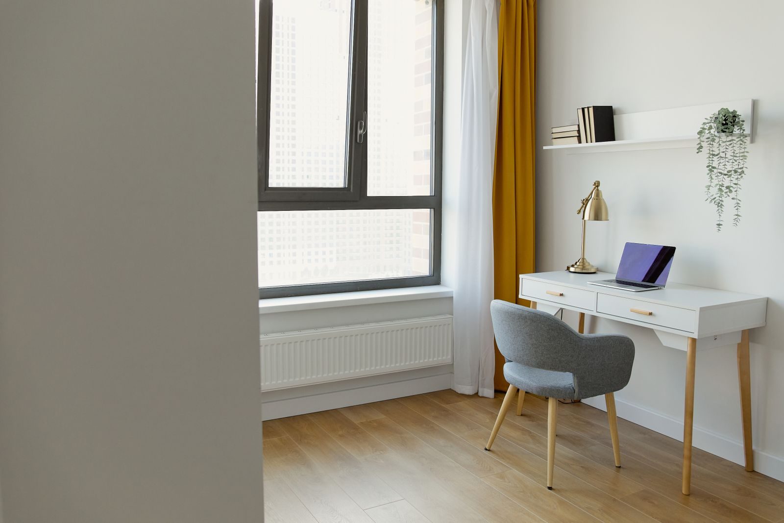 Home office claro e minimalista com mesa, cadeira, janela de cortinas amarelas e piso de madeira