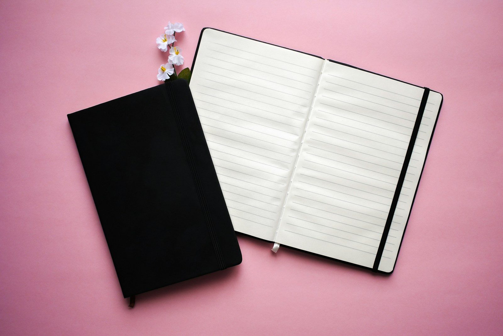 Caderno com caneta e flor sobre fundo rosa