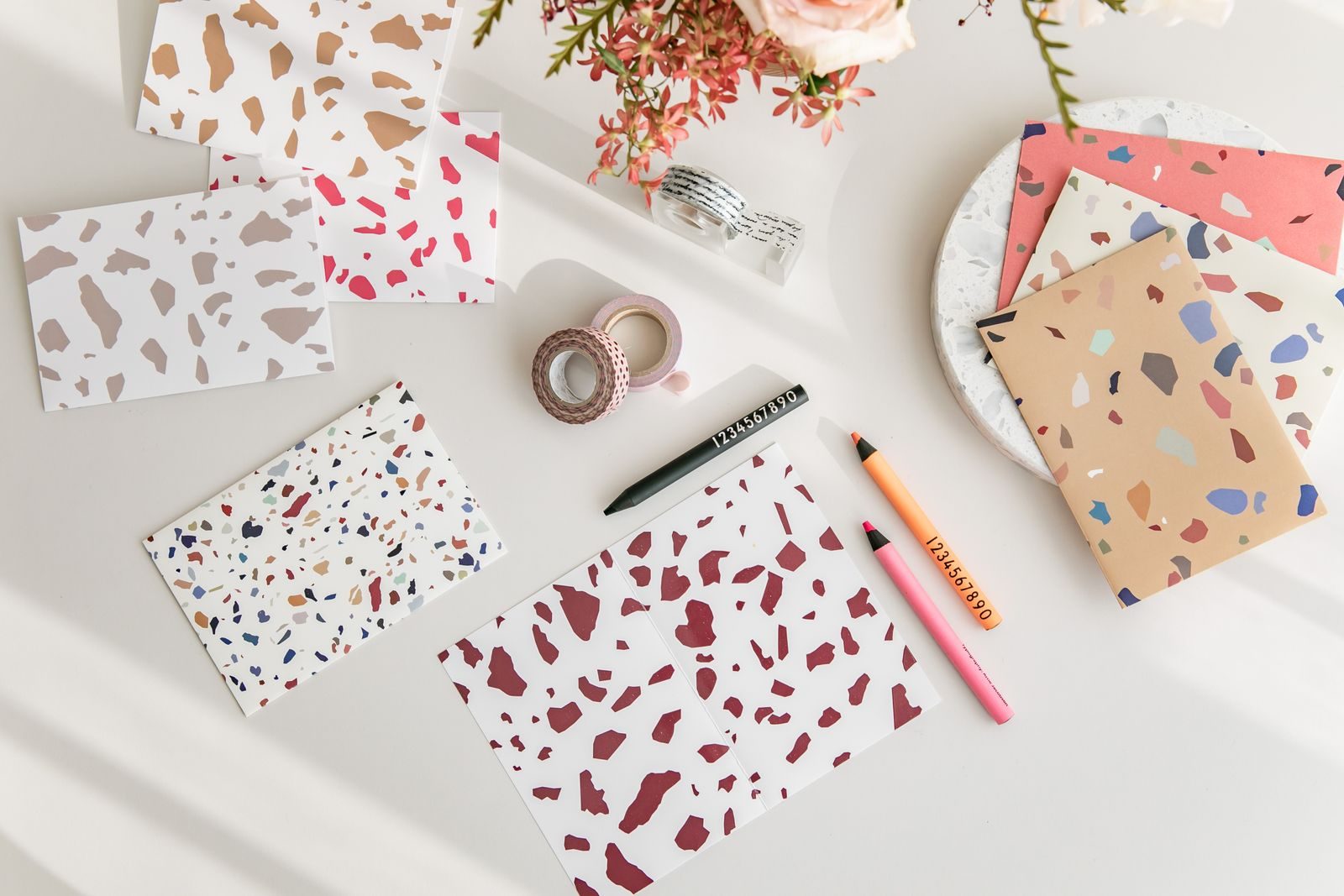 Papelaria com estampa terrazzo e flores rosa sobre mesa branca