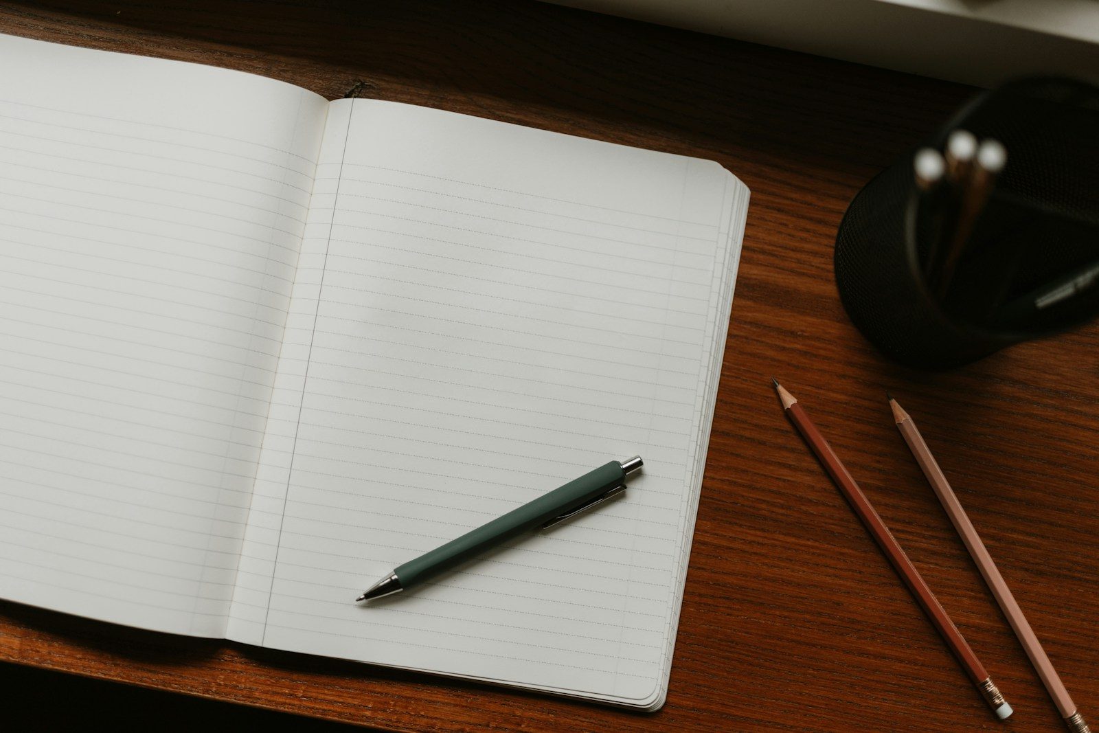 Caderno aberto com caneta e lápis sobre a mesa