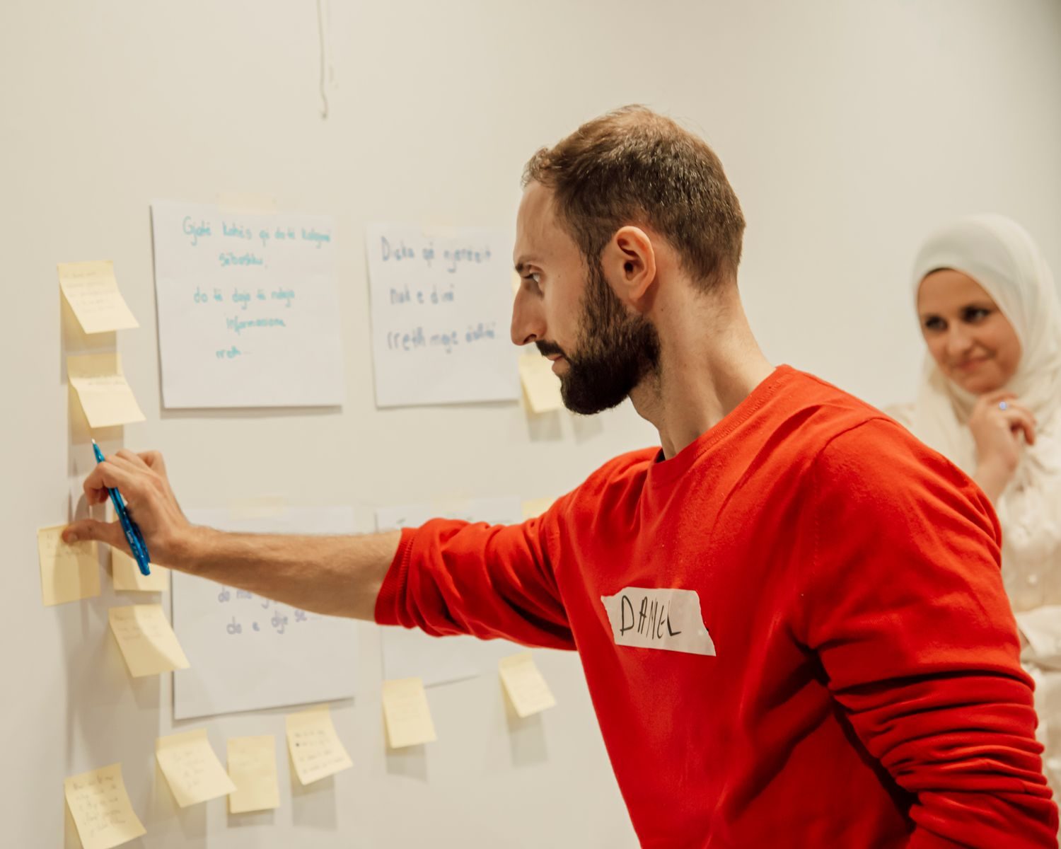Homem e mulher colaborando com post-its na parede durante uma sessão criativa