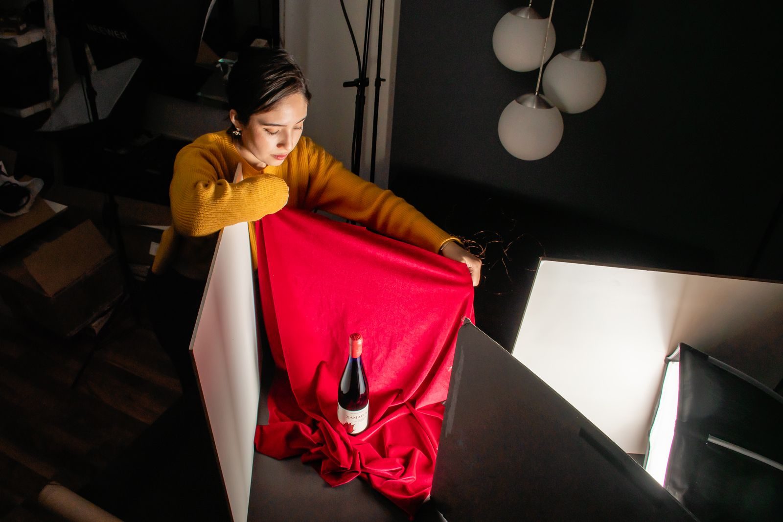 Fotógrafo montando cena com garrafa de vinho e tecido vermelho sob iluminação controlada no estúdio