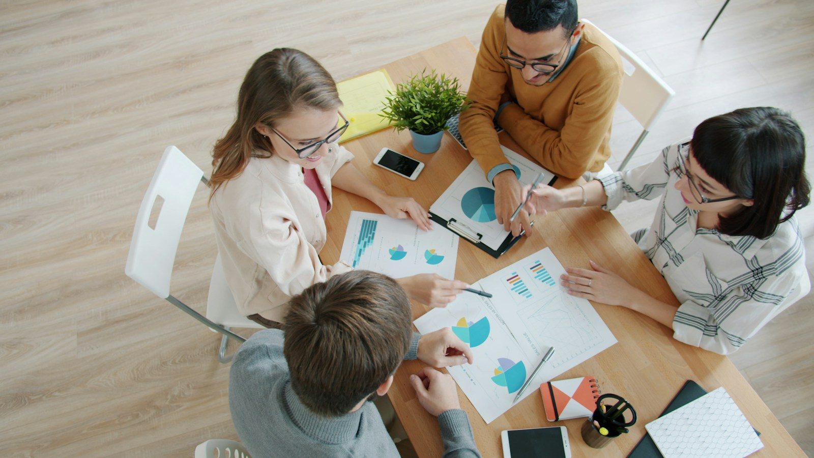 Quatro pessoas colaborando ao redor de uma mesa com gráficos