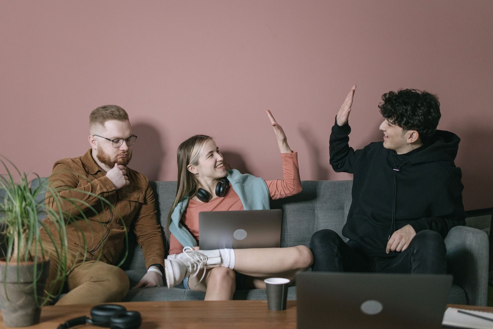 Três jovens colaborando em ambiente interno, se divertindo com notebooks e fones de ouvido