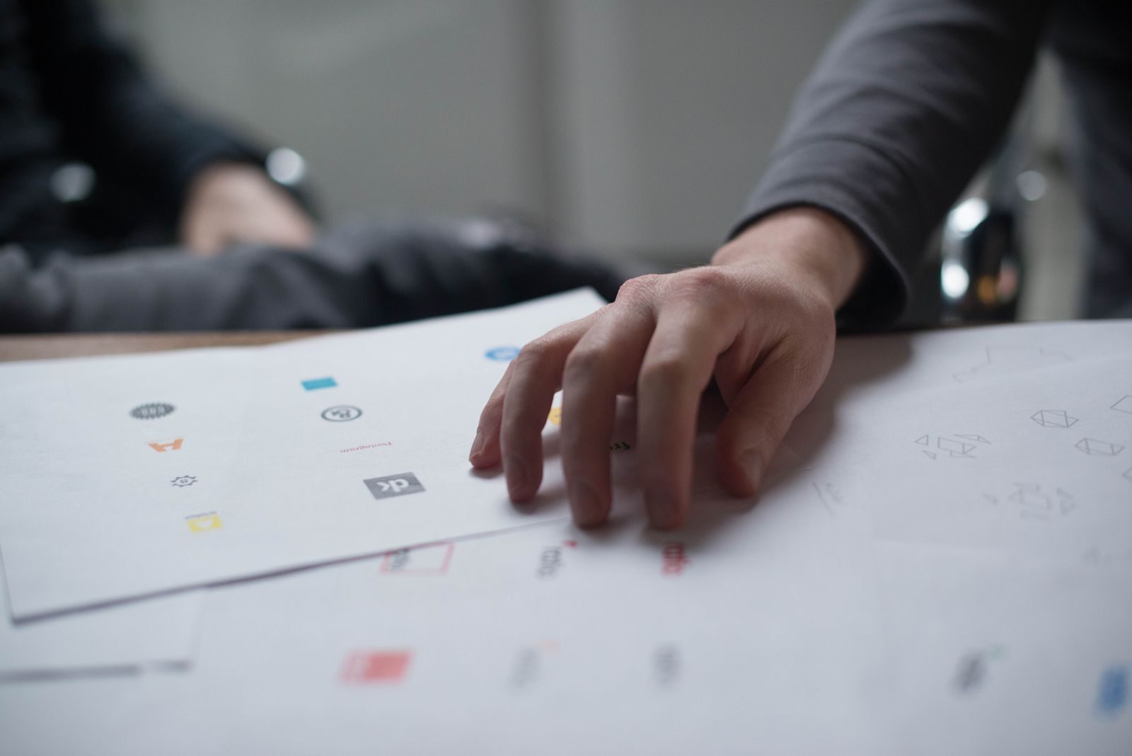 Mão analisando vários designs de logotipo em papel