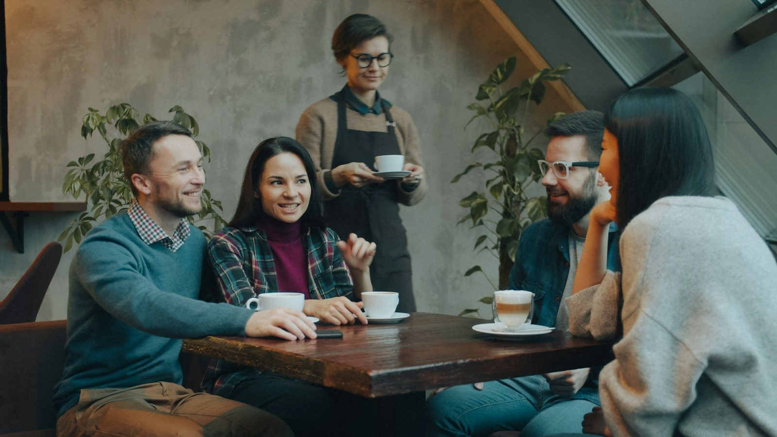 Grupo conversando em mesa de café enquanto um garçom se aproxima